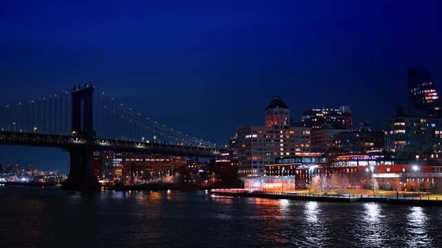 Luminous shores of the East River at night from the waterscape. Approaching the Manhattan Bridge in New York City, US.