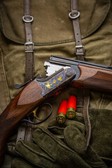 Luxury hunting shotgun with gold engraving, shells, and gloves on a canvas back © solidmaks