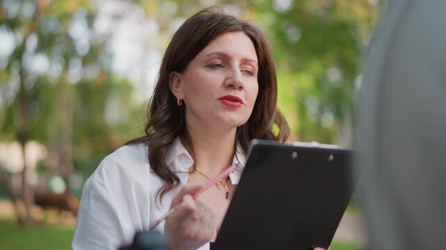 Caucasian woman reviewing mandate decree outdoors studying clipboard, offering legal counsel to unseen client, careful analysis of policy language, calm professional demeanor, lifestyle focused