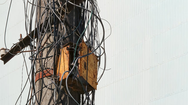 Electrical pole with tangled wires and rusty junction box in urban setting