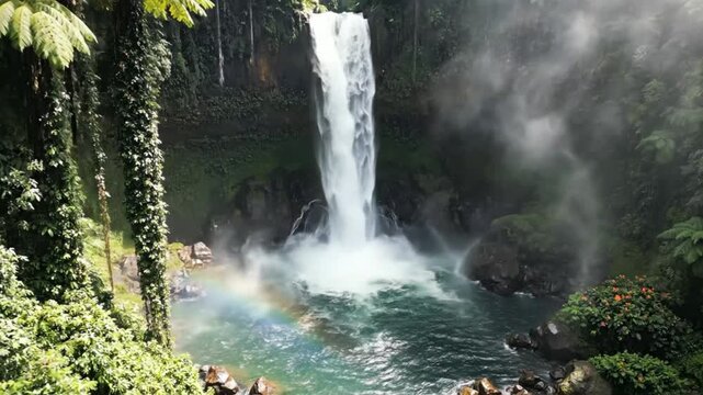 Scenic and stunning waterfall cascading into clear turquoise water with a colorful rainbow at the bottom