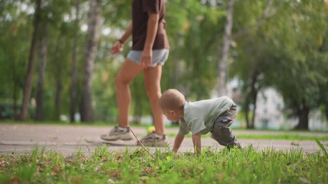 Toddler crawling then walking across pavement toward soccer ball, independent exploration and joyful kick attempt, caregiver watching nearby under green trees, lifestyle decree celebrating early