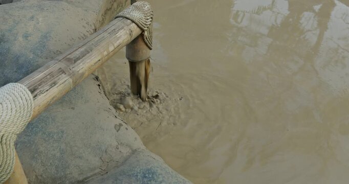 mud flows from a bamboo pipe into a mud bath, spa complex at sunset, baths with different herbs and flowers, abundant vegetation with flowers