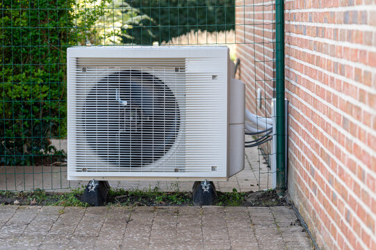 Outdoor unit of a modern air source heat pump installed next to a brick wall of a residential house. Energy-efficient heating system and renewable energy technology for sustainable home climate 