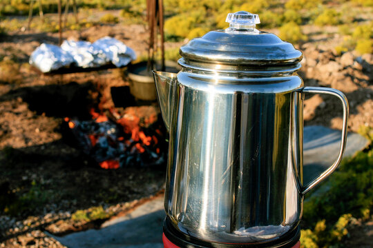Metal Coffee Pot Brewing Coffee Next to a Campfire in Outdoor Setting