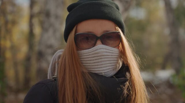 Woman walking through forest. An alert woman moving in nature setting. Veiled woman with backpack pacing through dense forest. Woman wearing sunglasses and scarf taking brisk steps in wooded area