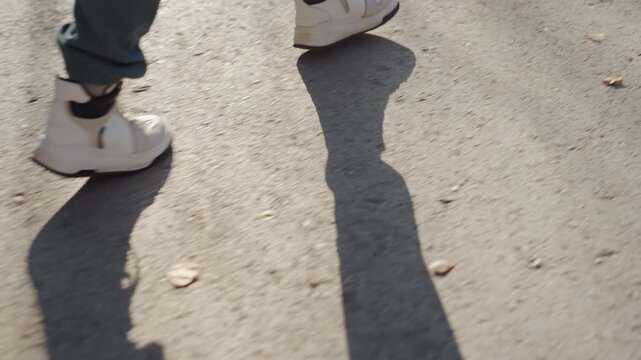 Closeup sneakers walking on pavement white sneakers green pants brisk steps long shadows groundlevel perspective escape vibe suspected thief fleeing street chase hurried pace tense atmosphere urban