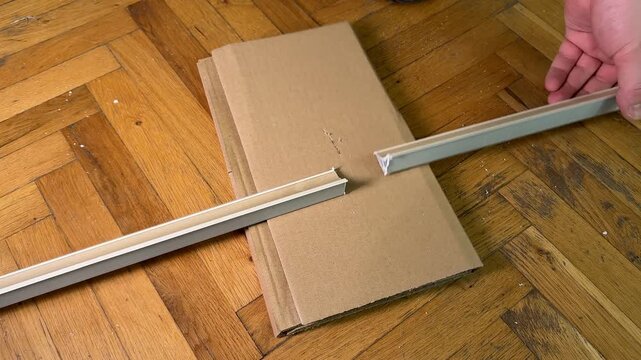 Close view of hands measuring cardboard with long metal ruler on wooden parquet floor, practical diy workspace, home renovation and packaging preparation