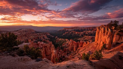 Naklejka premium Dramatic sunset illuminates a vast canyon landscape with striking terracotta formations, evoking a sense of timeless beauty and geological wonder.