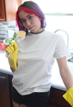 Young Woman With Colorful Hair Wearing Yellow Gloves Holding Cleaning Utensil in Bright Kitchen