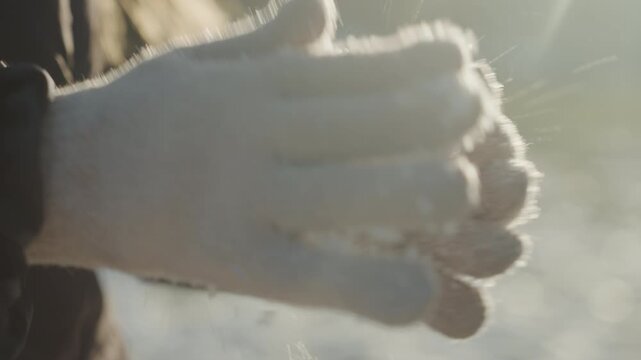 Closeup gloved caucasian hands rubbing snow, wool mittens catching sunlight, backlit flakes sparkling, textured fabric and gentle clap motion, subtle breath and tactile detail for cozy winter mood