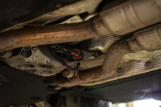 Underside view of car exhaust system with catalytic converters and pipes, showing emission control components installed along vehicle chassis.