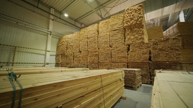 A large industrial warehouse featuring a forklift operating among stacks of dried wooden planks prepared for further furniture or flooring production
