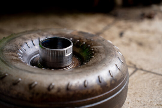 Top view of a used torque converter from an automatic transmission placed on a workshop floor, showing metal housing and central hub.