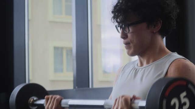 Medium shot of Asian man breathing heavily while doing final reps of bicep curls during upper body workout in gym