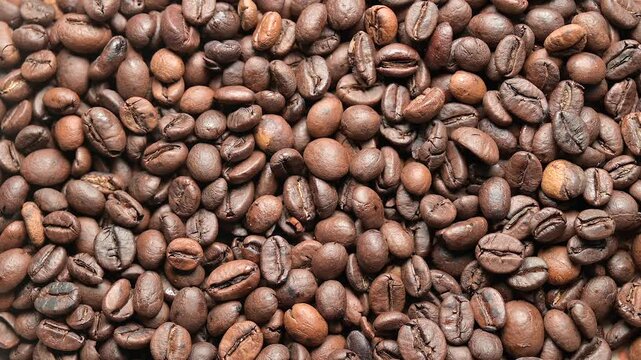 Top view close-up video of roasted coffee beans with a rotating motion creating a dynamic textured pattern. Rich brown tones and detailed surface highlight aroma, flavor and coffee culture