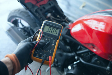 mechanic with multimeter checking the voltage level of a motorcycle © Artvibe