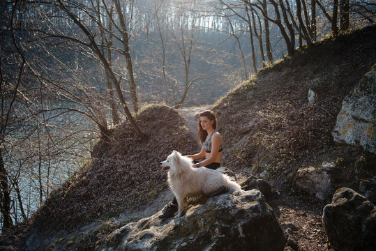 Woman in athletic wear with fluffy white dog on rocks in forest setting