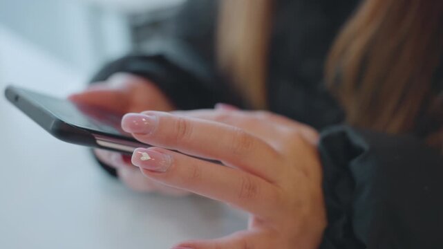 Closeup hands on phone, cafe table commuter taps screen with manicured nails, jacket sleeve visible shallow focus bokeh creates tense atmosphere suggesting potential snatcher and theft risk emphasis