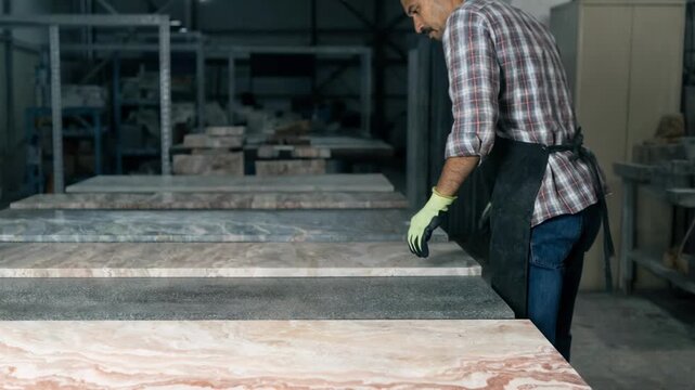 Stone slabs laid out dry on a workbench undergo thorough visual inspection by a technician focusing on natural color patterns and surface smoothness for quality assurance.