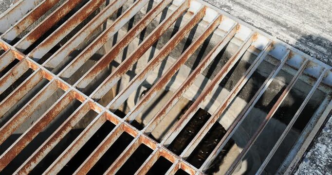 Rusty metal grate over a drainage channel, top view with sunlight and shadows. Industrial, urban decay, corrosion, structure, and grunge texture concept