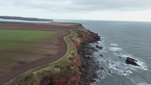 arbroath cliffs east coast of scotland dramatic epic rugged scenery forward movement drone shot red sandstone cliffs stormy sea waves over rocks