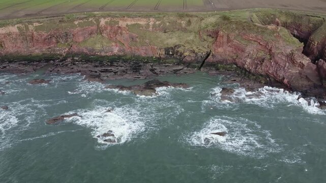 arbroath cliffs east coast of scotland dramatic epic rugged scenery static drone shot red sandstone cliffs stormy sea waves over rocks 