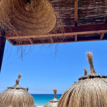 View from a beach bar through straw umbrellas to the turquoise ocean in Morro Jable, Fuerteventura