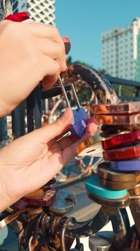 Hands of a traveler attaching a purple heart lock to a love bridge railing, symbolizing eternal commitment and romantic promises in an urban city setting under blue sky in da nang, vietnam
