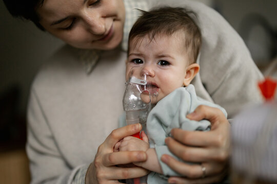 A mother gently holds her crying baby while giving them oxygen through a mask in a calm home setting