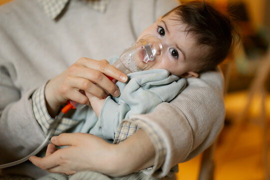 Parent gently holds baby using nebulizer for breathing treatment in warm cozy home setting