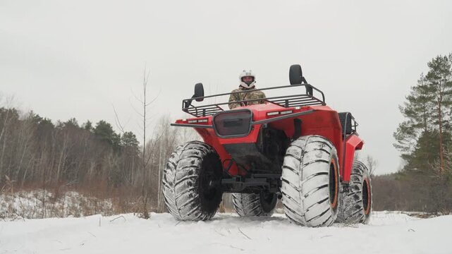 Red atv tearing through snow, rider in helmet launching small jump, high snow spray, low camera angle, pine forest background, heavy tread tires digging into frozen trail, powerful winter offroad