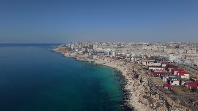 Panoramic drone view of Aktau city, located on the rocky shores of the Caspian Sea. The footage features modern high-rise residential complexes and developing urban infrastructure against the desert 