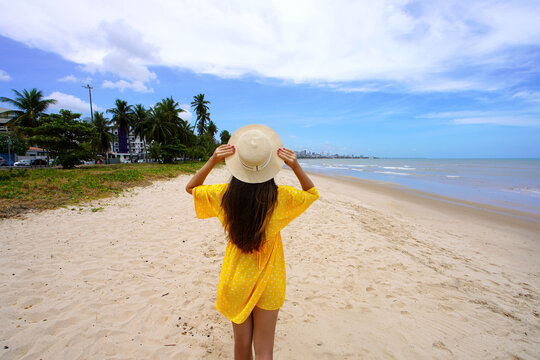 Young woman with yellow sundress walking Cabo Branco beach, Joao Pessoa, Brazil
