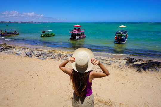Tourism in Maceio, Brazil. Back view of woman looking jangadas rafts going to natural swimming pools of Ponta Verde, Maceio, Brazil.