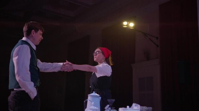 Amateur theatrical performance with costumed actors on dimly lit stage featuring simple props, table setting, and dramatic expressions during live indoor play