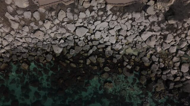 Mesmerizing top-down aerial view of the rocky Caspian Sea coast in Aktau. Crystal clear turquoise water washes over large boulders and scenic stones. Bright sunny day in Mangystau, pristine wild 