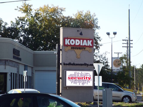 Ottawa, Ontario, Canada &ndash; July 26, 2025: The "Kodiak Security pylon sign" features a digital display showing a security word cloud, located near parked cars and trees" on Riverside Dr.
