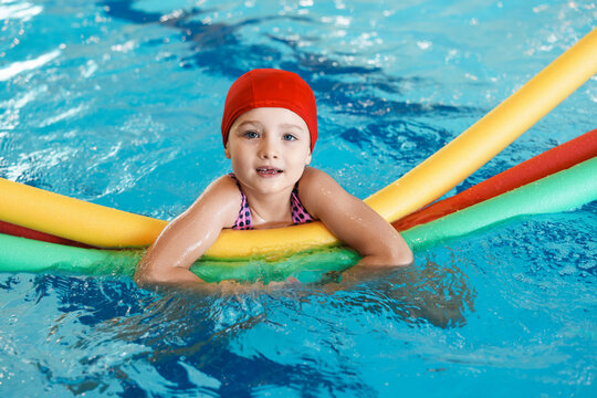 Cute little girl swimming with water noodles during lesson in pool