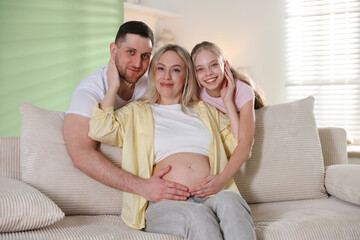 Obraz premium Pregnant woman with her daughter and husband on sofa at home