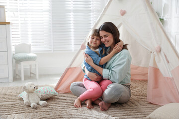 Mother and her daughter near toy wigwam at home, space for text © New Africa