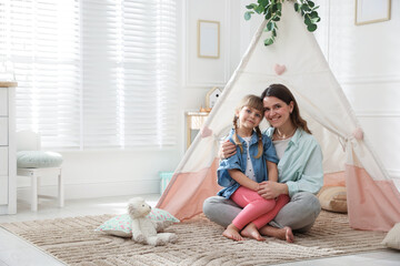 Mother and her daughter near toy wigwam at home, space for text © New Africa