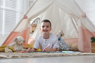 Little boy drawing in sketchbook near toy wigwam at home © New Africa