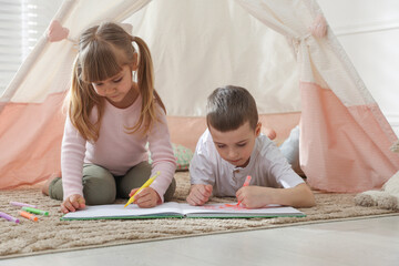 Little kids drawing in sketchbook together near toy wigwam at home © New Africa