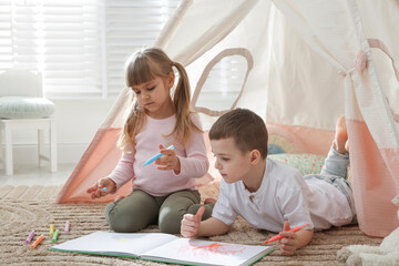 Little kids drawing in sketchbook together near toy wigwam at home © New Africa