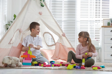 Little kids playing with building blocks near toy wigwam at home © New Africa