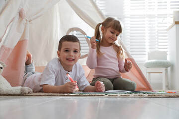 Little kids drawing in sketchbook together near toy wigwam at home © New Africa