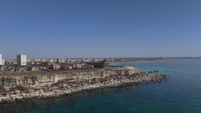 Dynamic aerial drone approach to the elite coastal area of Aktau. View of modern villas, high-rise residential complexes, and a well-maintained pedestrian promenade on the rocky shores of the Caspian 