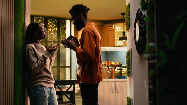 Black boyfriend seeing her girlfriend laugh at mobile phone screen, being suspicious about a potential affair, worrying about infidelity and dishonesty. Controlling toxic man in rage, bullying.