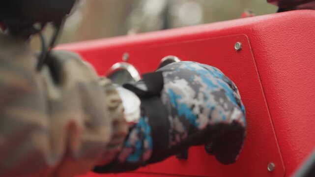 Gloved hand starting red atv dashboard, camouflage sleeve twists ignition key on textured red control panel with gauges and switch, closeup of rider preparing extreme offroad ride through forest